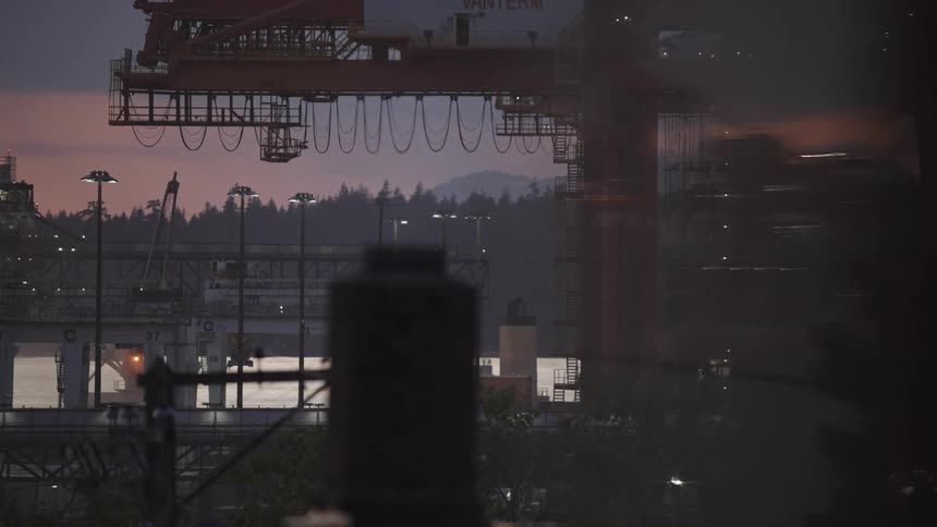 Industrial crane stands out at dusk near the illuminated port