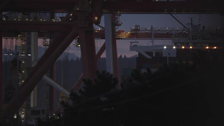 Industrial structures lit at dusk with containers and cranes in view
