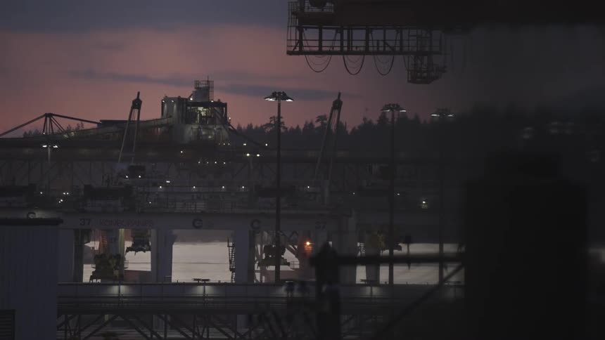 A container shipping port is busy with cranes operating at dusk