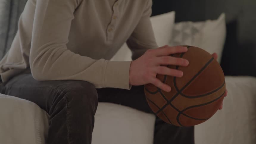 A person sits on a bed spinning a medium sized ball in their hands