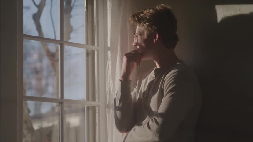 A man stands by a window lost in thought indoors
