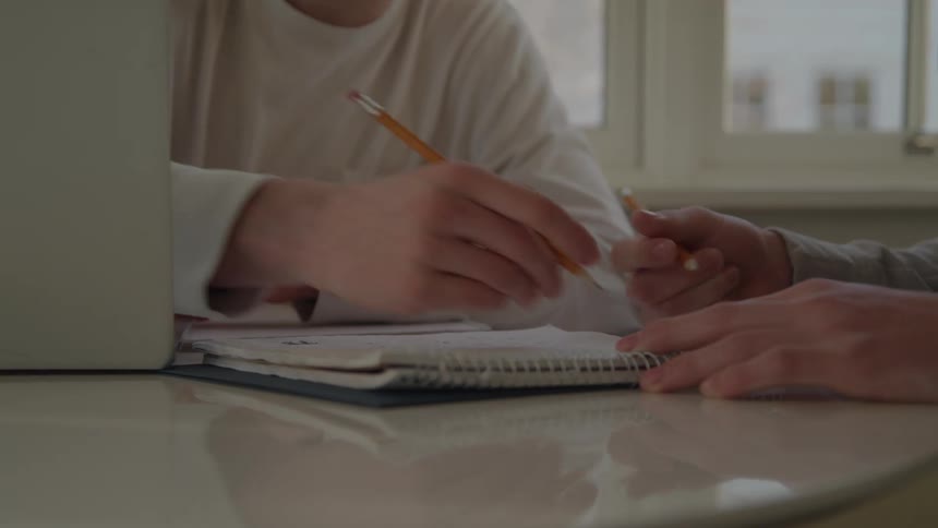 Hands write in a notebook during a collaborative study session