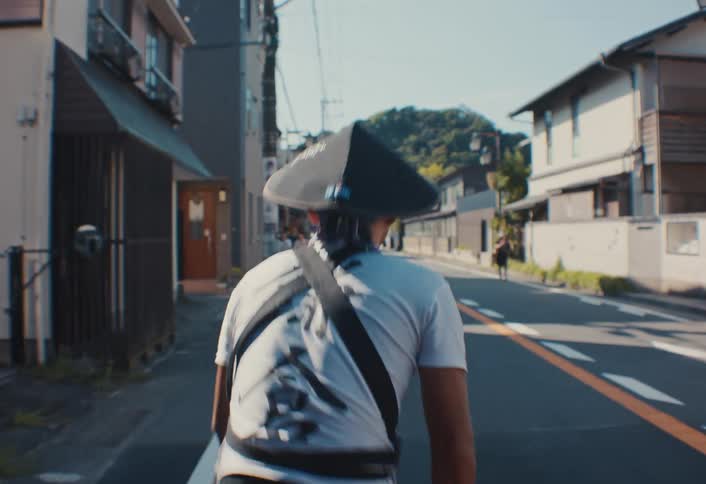 A man wearing a black hat with his back turned and running on an asphalt street