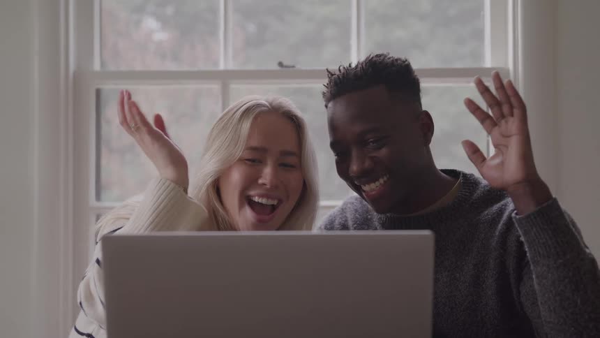 A man and woman smile and wave while video chatting on a laptop computer