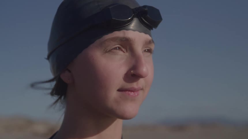 A young woman wearing a dark swim cap and goggles on their forehead looking off to the horizon