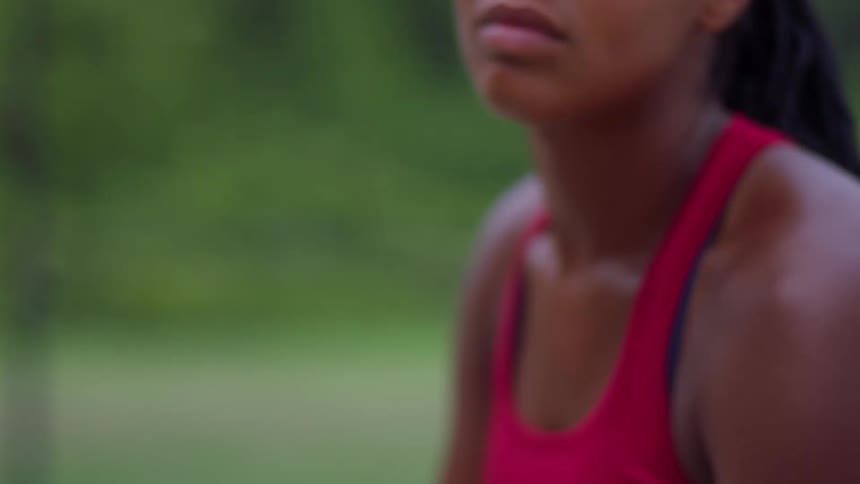 A womans lower face and shoulders as she breathes heavily before she rapidly raises her right arm out of the frame to play tennis