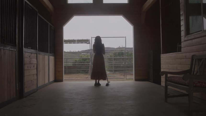 Woman stands in a barn holding a broom stick