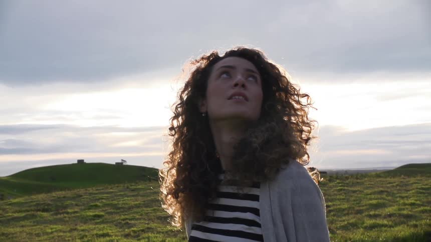 Curly hair woman walks looks up at the sky in the field