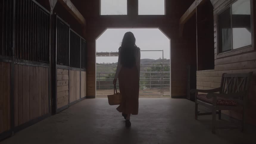 Woman walking through a stable carrying a straw basket