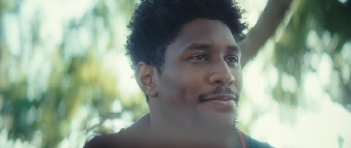 A man outdoors gazes off to the side with a soft optimistic smile