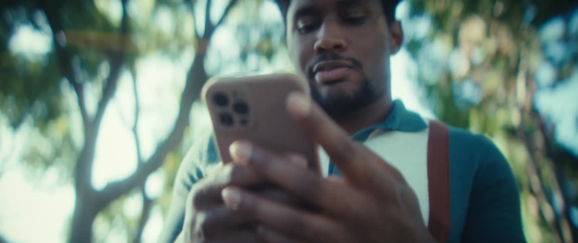 A young man holds and uses a mobile phone with both hands while standing outdoors