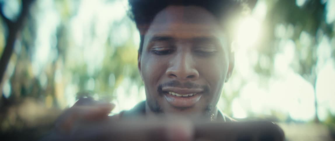 Man smiles slightly while looking at the phone under sunlight