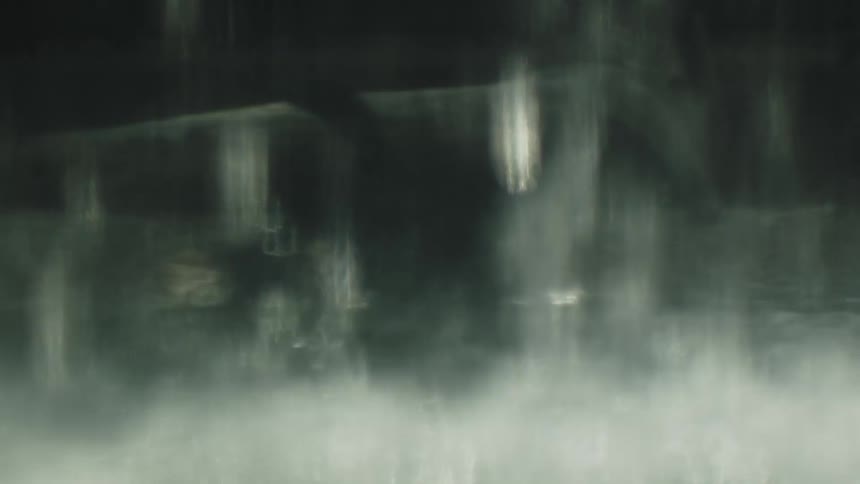 A bird flaps its wings beneath an overhang with water falling from it