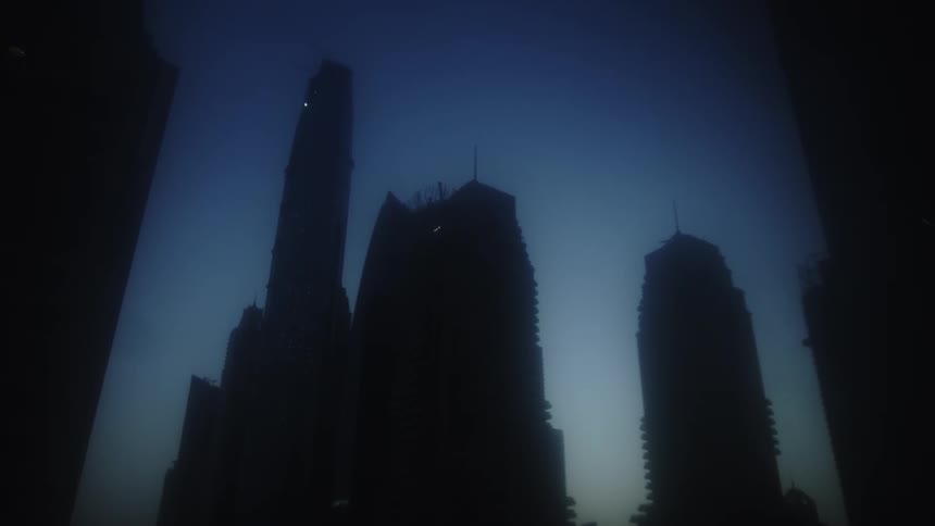 This shot features the silhouettes of three tall skyscrapers that rise dramatically against a dark deep blue twilight skythe buildings appear to be framed or viewed through a dark opening giving the shot a mysterious or slightly forebodin