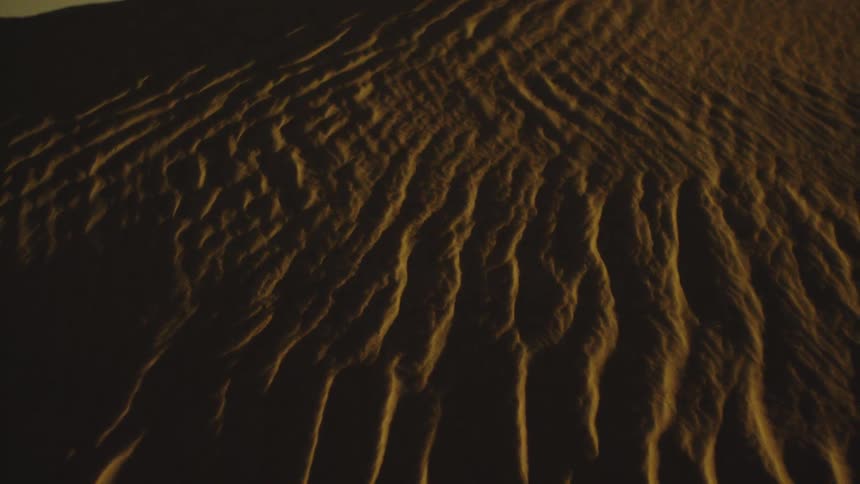 Wavy sand textures illuminated by golden light create striking patterns on the ground