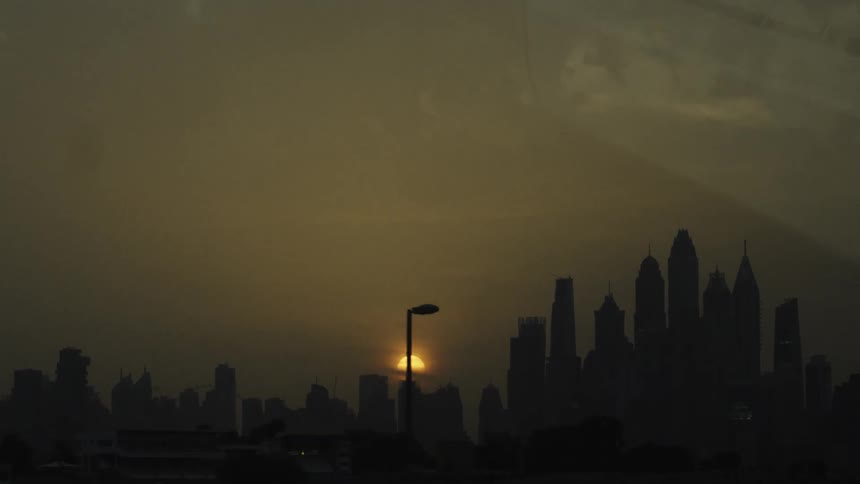 Sun sets behind skyscrapers tinting the urban sky with orange hues