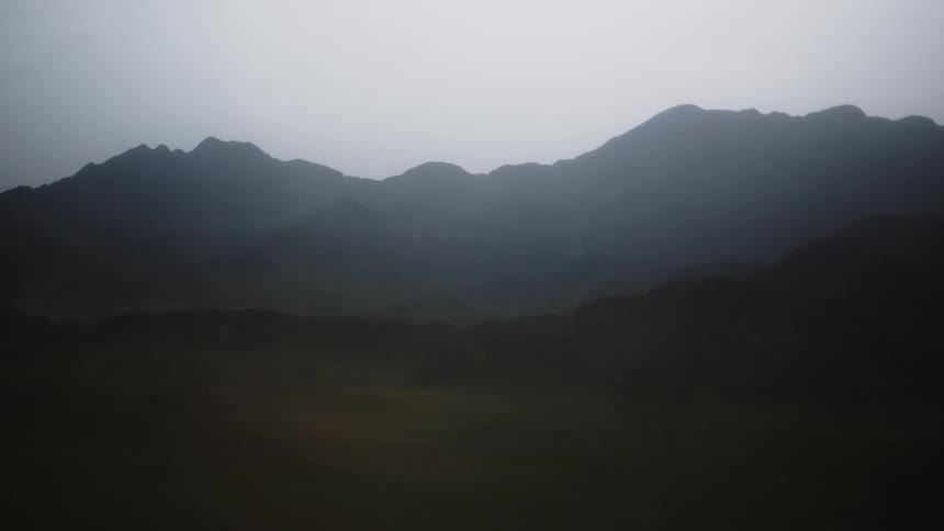 Moody mistdraped mountains under a flat gray sky everything softened by haze so the ridgelines fade from dark foreground to pale distance