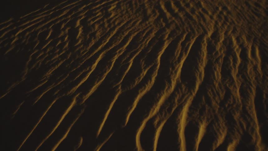 Wavy textures form in the sand illuminated by golden light