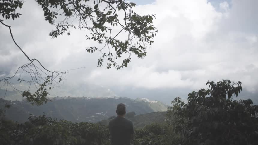 Person stands on hillside overlooking cloudy mountains