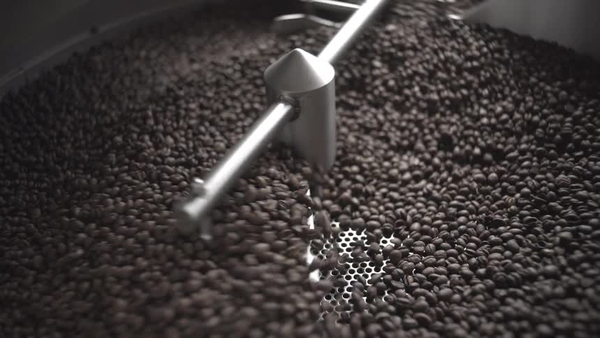 A close highangle view shows dark brown coffee beans being rapidly stirred and cooled by the silver metal paddles of an industrial coffee roaster machine