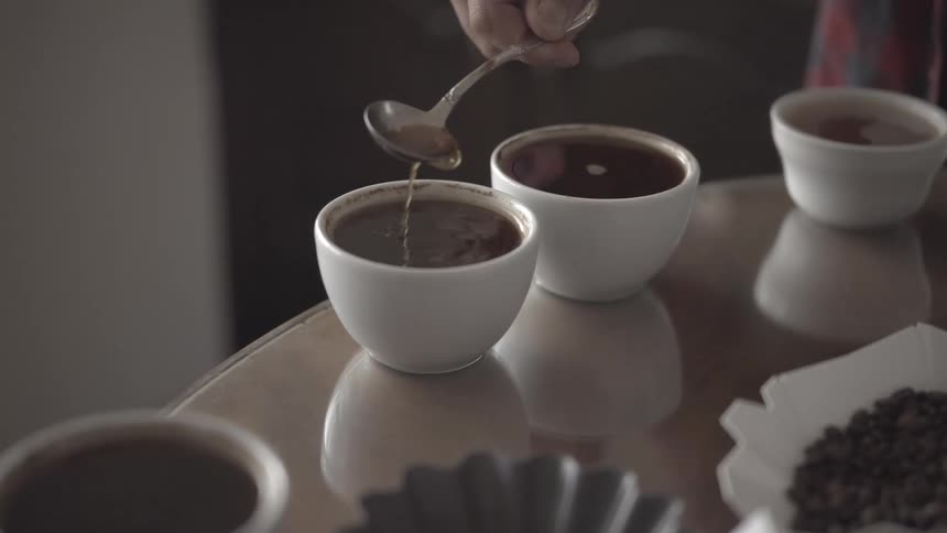 A person tastes coffee from a small white cup with spoon on a table