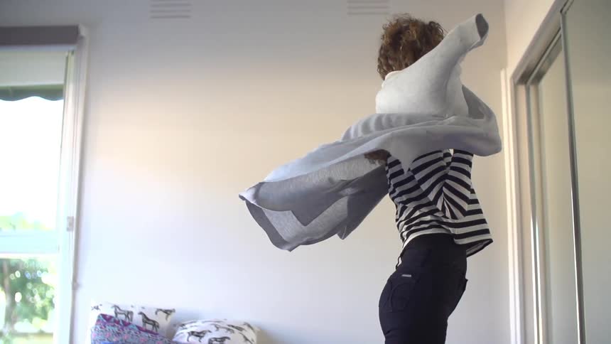 In slow motion, a woman flings a jacket over her shoulders, and starts to slide her arm into the arm of the jacket