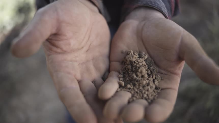 Close up of a man transferring soil between his palms while standing outdoors during daytime
