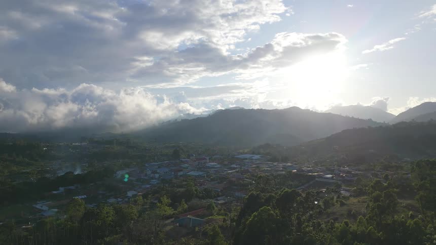 Green valley shelters buildings among mountains under a sky partially lit by the sun