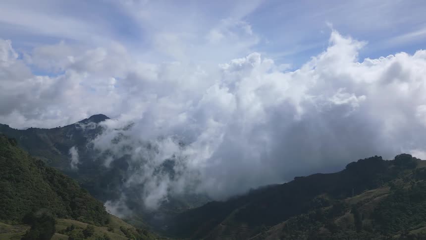 Thick clouds roll over the mountains under a blue sky