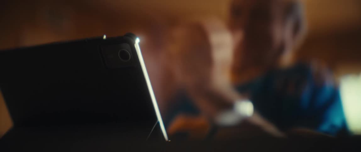 Elderly man clapping in the background while a tablet is prominently visible in the foreground