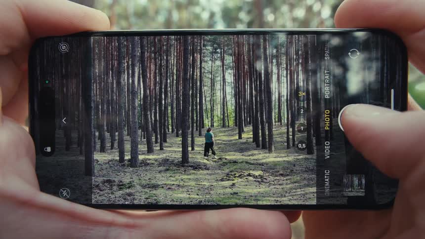 Pair of hands holding a smartphone and photographing a person walking through a forest