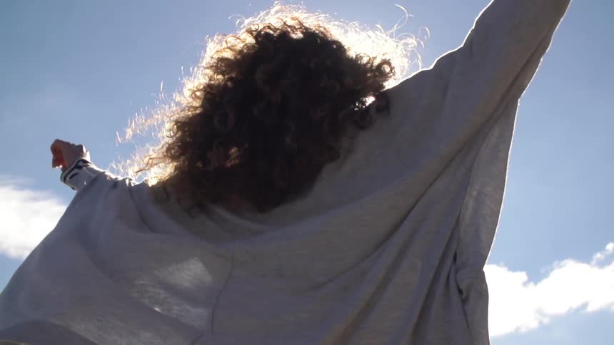 A young woman raising her arms toward the sky on a sunny day