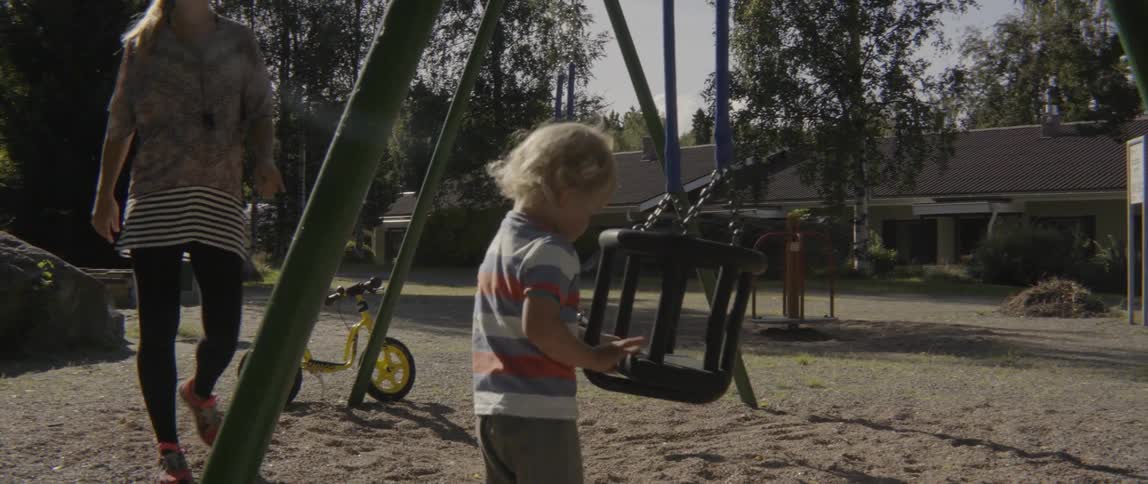 Young toddler boy practicing his motor skills while playing with a playground swing set.