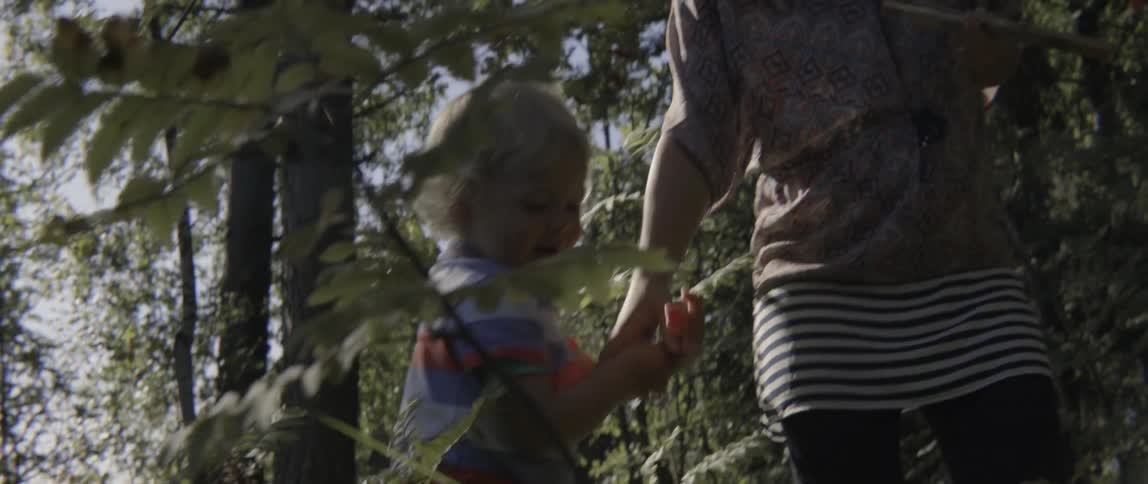 Happy toddler boy jumping with assistance from his mother during a sunny forest outing