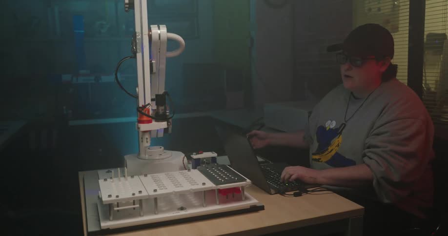 The woman controls the robotic arm with a laptop