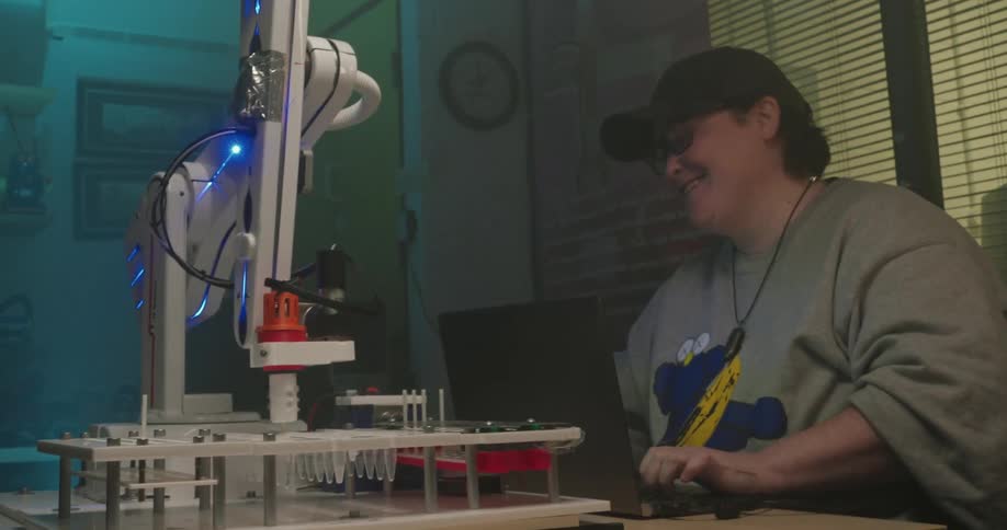 A young person laughing while working with a laptop and robotic arm in lab