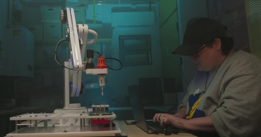 Person works on a laptop beside a robotic arm in a laboratory