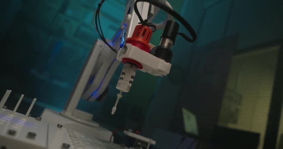 A small precise robotic arm performing a task over a series of small electronic components in a blue lit lab
