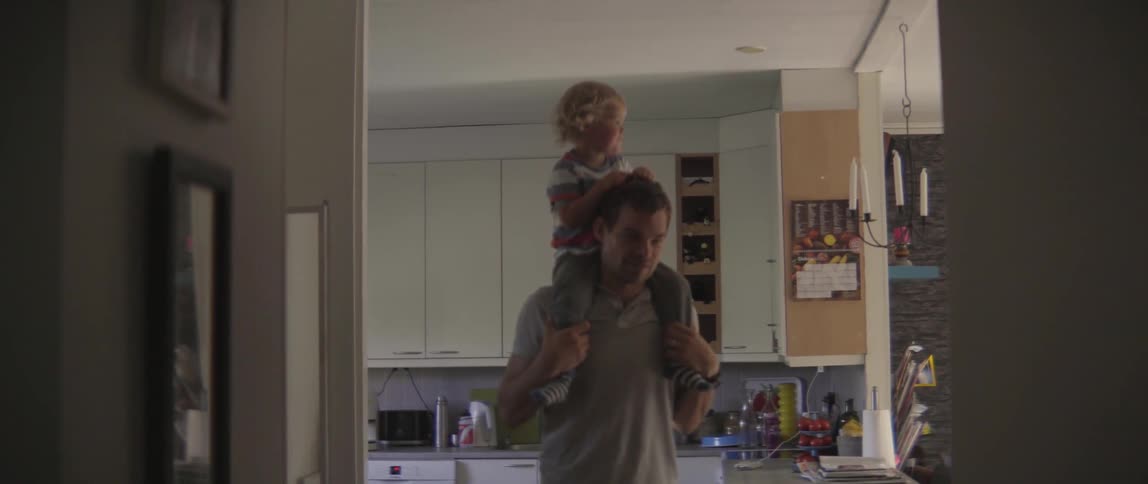 Young father walking through the house while carrying his smiling toddler son on his shoulders.