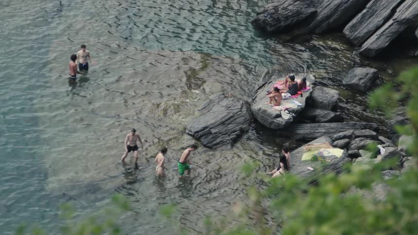 People swim and relax among rocks in a shallow coastal area
