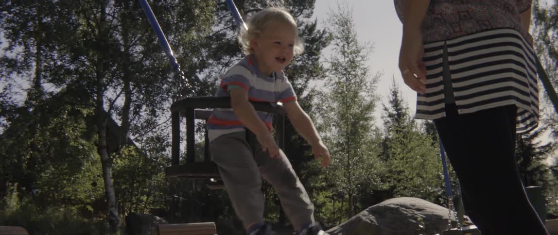 Young toddler boy being pushed by his mother during a fun outdoor play session.