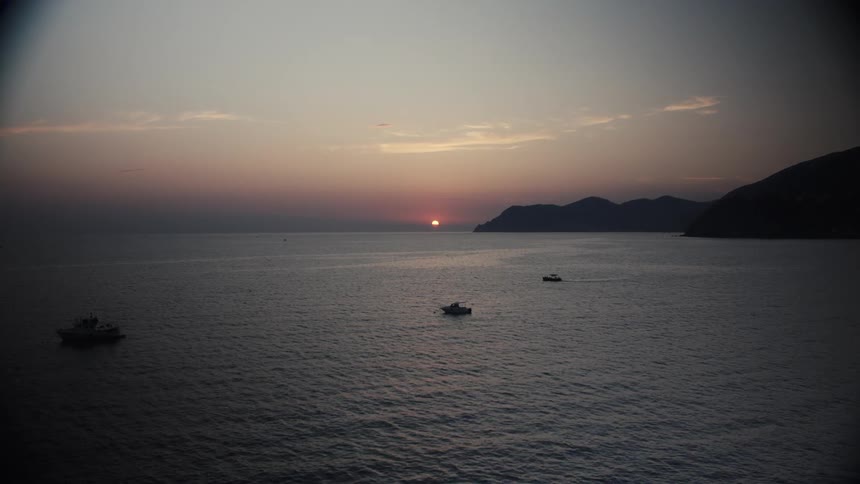 Sun setting on the horizon over the sea with boats scattered across the calm water