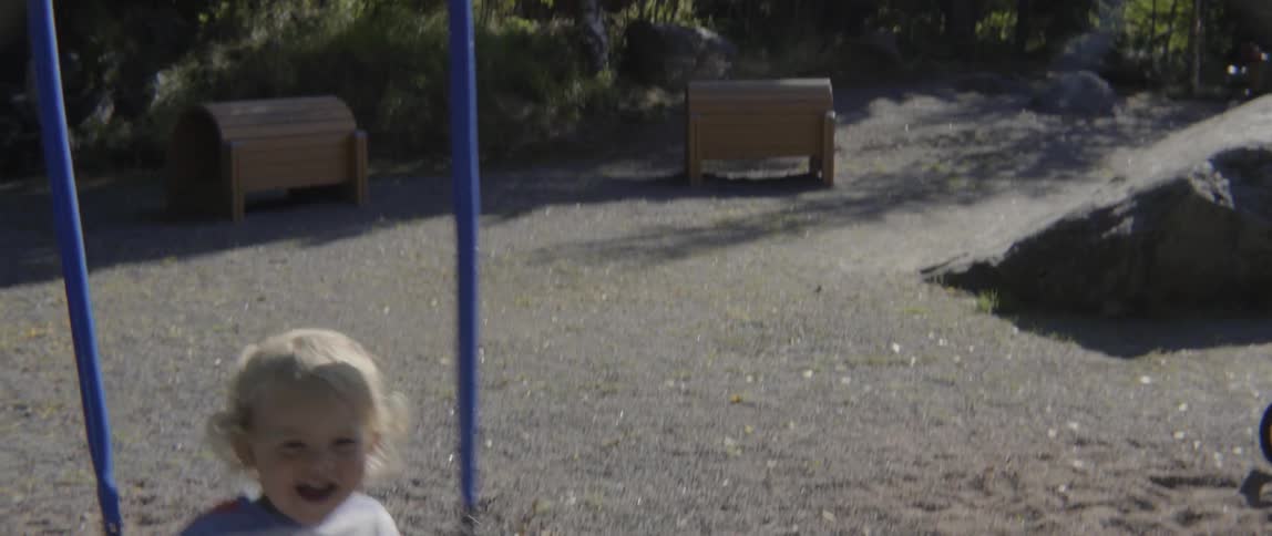 A happy young toddler boy smiles and laughs while being pushed on a swing.