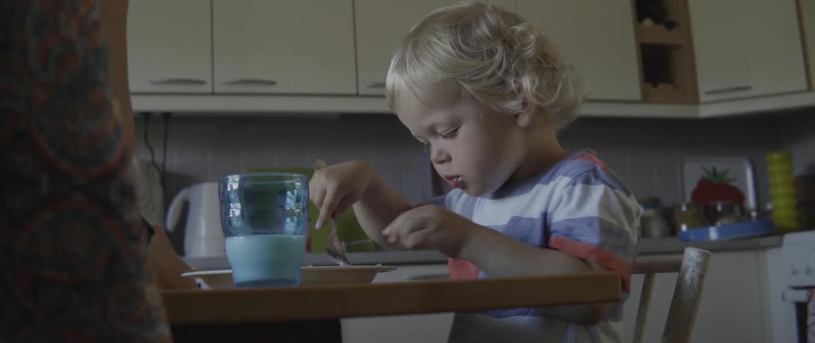 Happy toddler boy having a meal while sitting at the table indoors in summer.