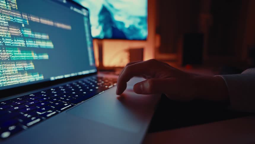 A developer coding on a laptop in a dimly lit room