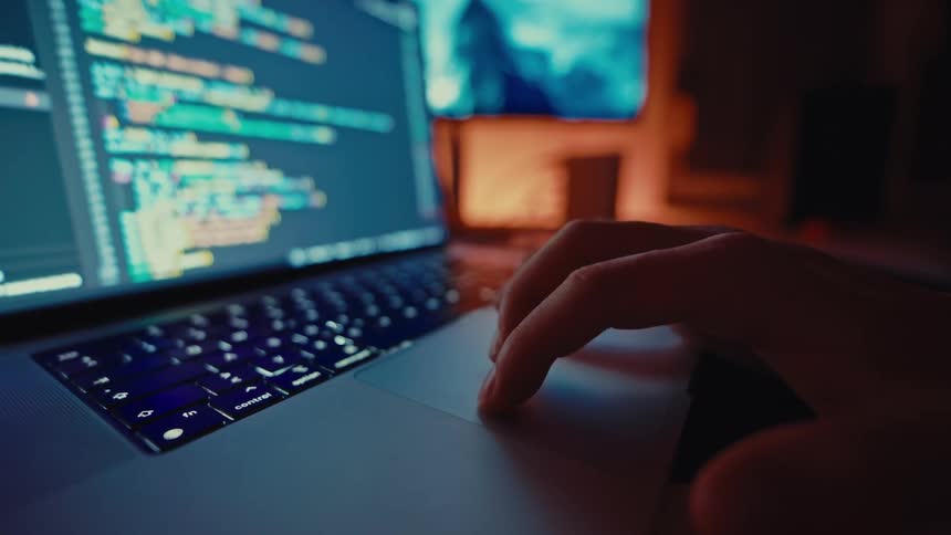 Developer scrolls laptop trackpad with colorful code on screen