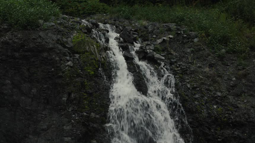 Waterfall cascading down dark rocks surrounded by green vegetation
