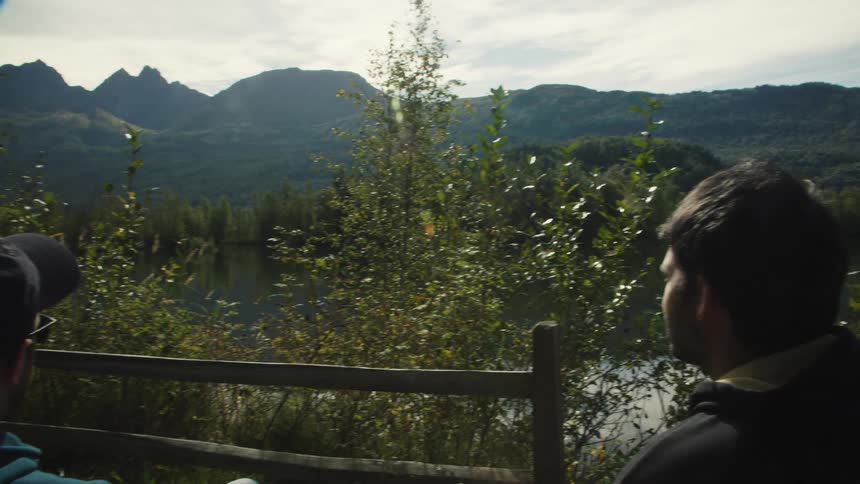 Two men sitting and admiring a beautiful landscape with a large lake mountains and trees in the background