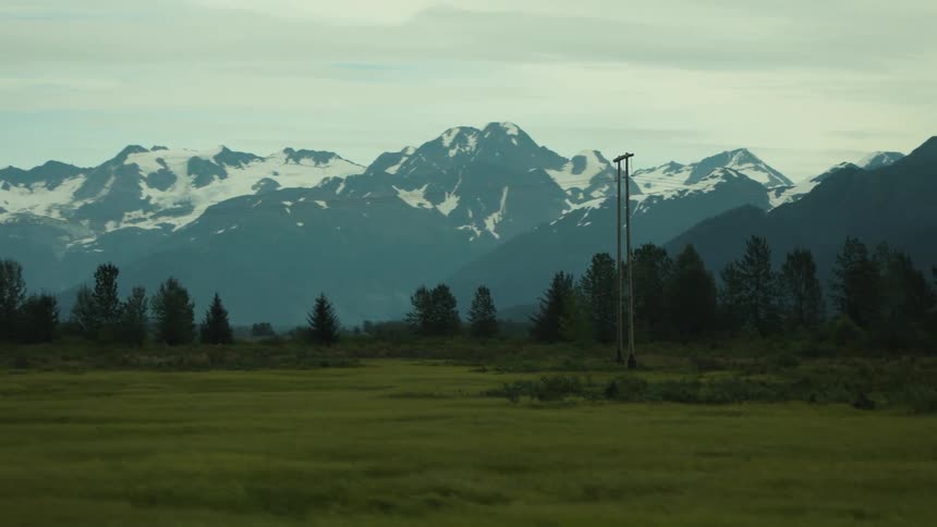 The green field is before the snow covered mountains