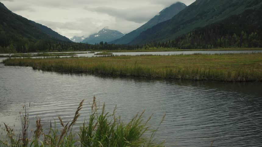 A river winds through a valley surrounded by hills and distant mountains